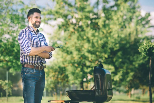 Handsome man preparing barbecue for friends. man cooking meat on barbecue - Chef putting some sausages and pepperoni on grill in park outdoor - Concept of eating outdoor during summer time. — Stock Photo, Image