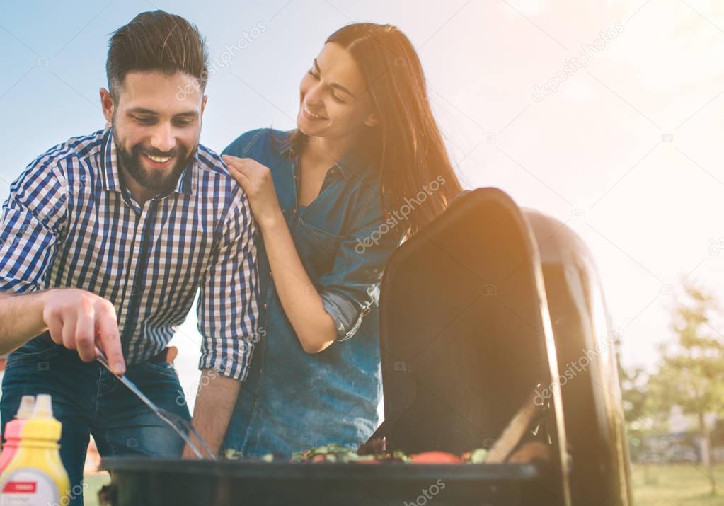 Friends making barbecue and having lunch in the nature. Couple having fun while eating and drinking at a pic-nic - Happy people at bbq party.