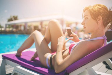 Sıcak havuzda bikinili genç ve güzel bir bayan tatil köyünde cep telefonuyla konuşuyor..