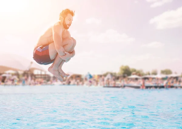Hombre en pantalones cortos azules y rojos saltando en la piscina en el día soleado. Disfrutando de la fiesta en la piscina con amigos —  Fotos de Stock