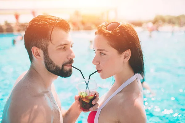 Pareja joven junto a la piscina. Hombre y mujeres bebiendo cócteles en el agua — Foto de Stock