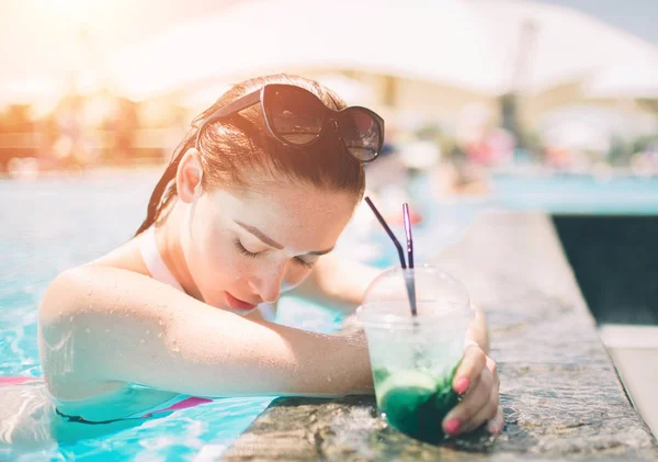 Chica morena con cócteles relajante en la piscina. Mujer sexy en bikini disfrutando del sol de verano y bronceado durante las vacaciones en la piscina con bebida . — Foto de Stock