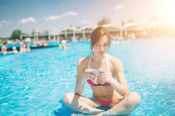 Joven hermosa mujer sonriente en bikini en la piscina caliente en el resort y hablar en el teléfono móvil . — Foto de Stock