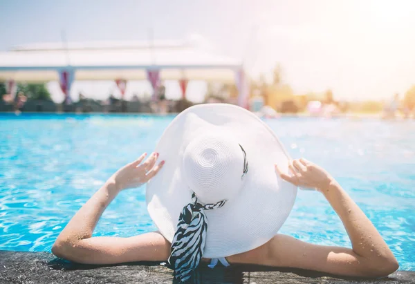 Mujer joven feliz en sombrero grande relajarse en la piscina, viajar cerca de la playa en la puesta de sol. Concepto verano —  Fotos de Stock