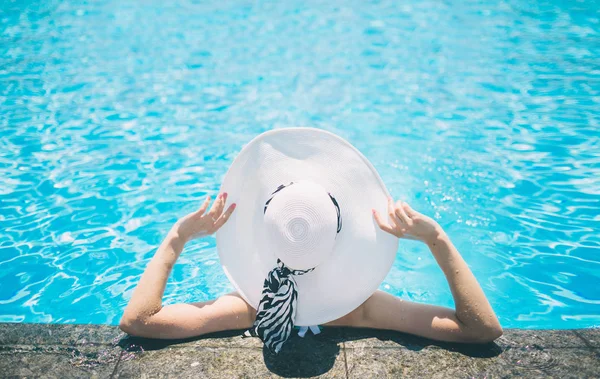 Mujer joven feliz en sombrero grande relajarse en la piscina, viajar cerca de la playa en la puesta de sol. Concepto verano —  Fotos de Stock