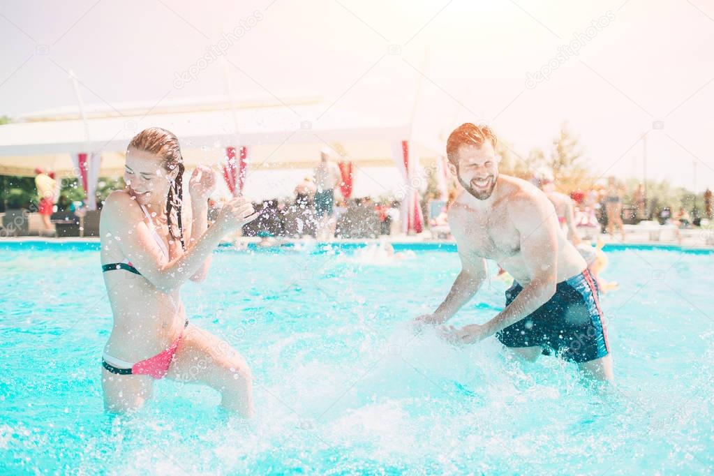 Cheerful youthful guy and lady resting while swimming pool outdoor. Couple in water. Guys do summer sephi.