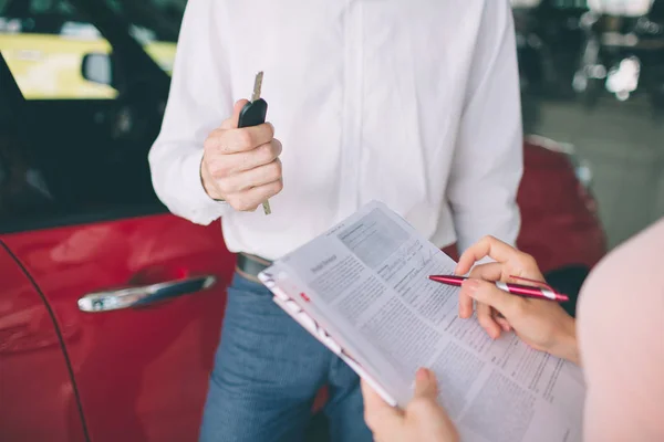 Vendedor de coches amigable hablando con una mujer joven y mostrando un coche nuevo dentro de la sala de exposición Firma del contrato . — Foto de Stock