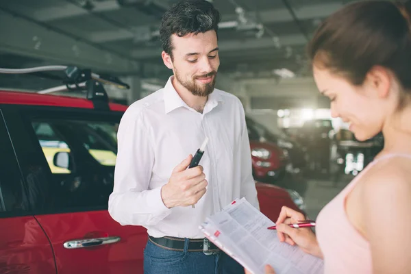 Vendedor de coches amigable hablando con una mujer joven y mostrando un coche nuevo dentro de la sala de exposición Firma del contrato — Foto de Stock