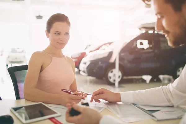 Amichevole venditore di auto parlando con una giovane donna e mostrando una nuova auto all'interno dello showroom Firma del contratto . — Foto Stock