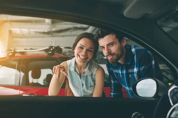 Hermosa pareja joven de pie en el concesionario elegir el coche para comprar — Foto de Stock
