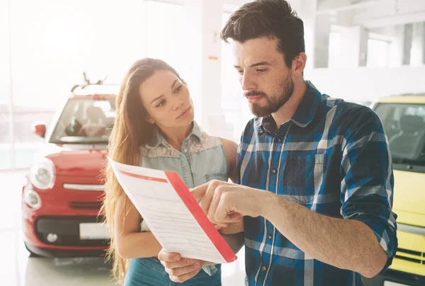 Beau jeune couple debout à la concession en choisissant la voiture à acheter — Photo