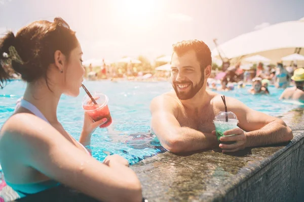 Pareja joven junto a la piscina. Hombre y mujeres bebiendo cócteles en el agua . — Foto de Stock