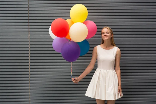 Glad ung kvinna med färgglada ballonger på en gata nära grå - utomhus sommaren koncept — Stockfoto