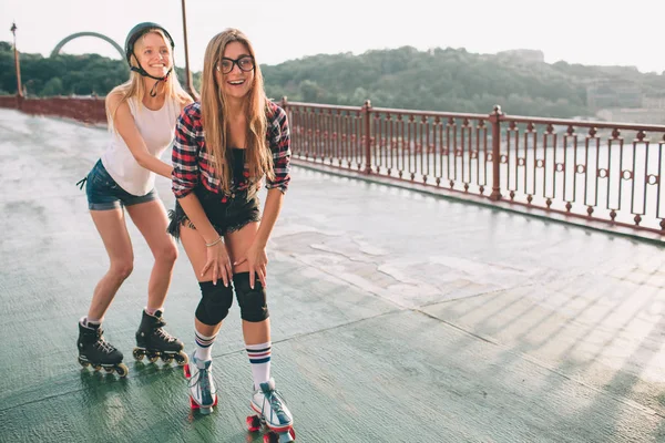 Dos mujeres jóvenes delgadas y sexy y patines. Una hembra tiene patines en línea y la otra tiene patines cuádruples. Las niñas viajan en los rayos del sol —  Fotos de Stock