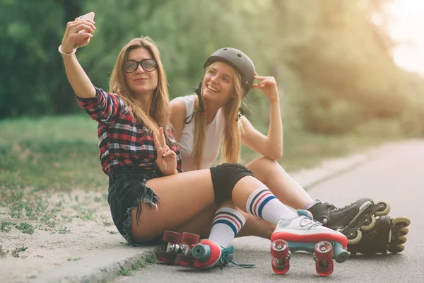 Duas mulheres jovens magras e sensuais e patins. Uma fêmea tem patins em linha e a outra tem patins quádruplos. Meninas passeio nos raios do sol . — Fotografia de Stock