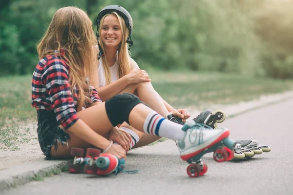 Dos mujeres jóvenes delgadas y sexy y patines. Una hembra tiene patines en línea y la otra tiene patines cuádruples. Las niñas viajan en los rayos del sol . — Foto de Stock