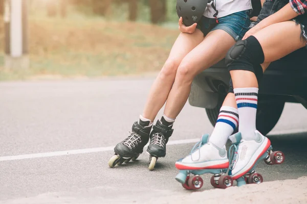 Dos mujeres jóvenes delgadas y sexy y patines. Una hembra tiene patines en línea y la otra tiene patines cuádruples. Las niñas viajan en los rayos del sol —  Fotos de Stock