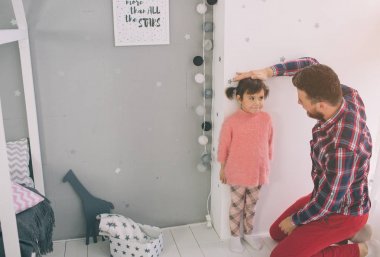 Baban duvardaki bebek boyunu ölçmek. Sevimli küçük kız ve yakışıklı genç babası birlikte childs odada oynayan