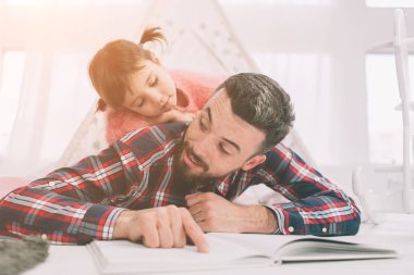 Baba yatak odasında yerde yatarken kızına bir kitap okuyor. Şirin küçük kızı ve yakışıklı genç babası çocuk odasında birlikte oynuyorlar.