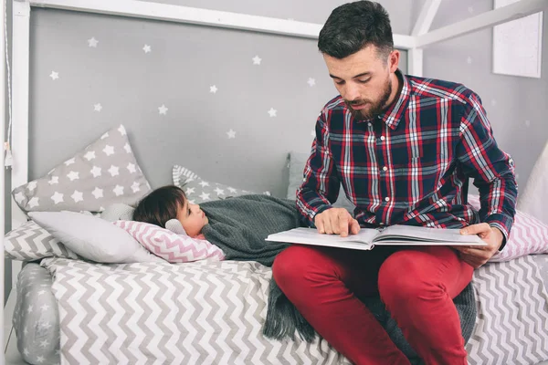 Отец читает книгу своей дочери, лежа на кровати в спальне. — стоковое фото