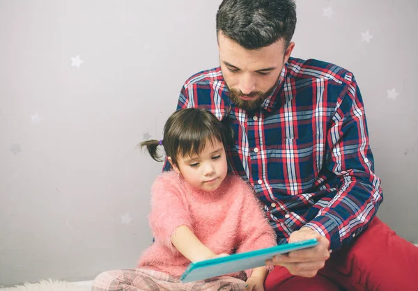Милая маленькая девочка и ее красивый отец используют цифровой планшет и улыбаются, сидя дома . — стоковое фото