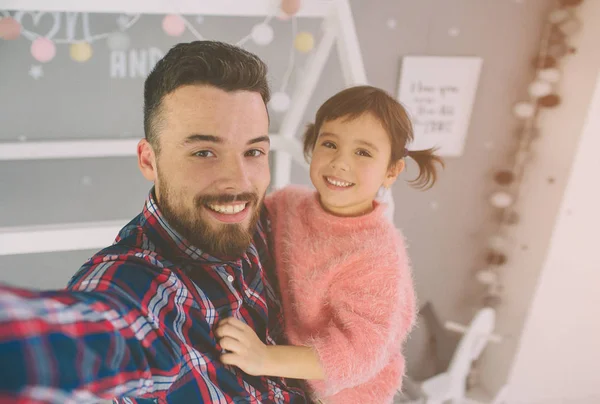 Roztomilá dcerka a její hezký mladý táta si spolu hrají v dětském pokoji. Táta a dítě spolu tráví čas, zatímco sedí na podlaze v ložnici. — Stock fotografie