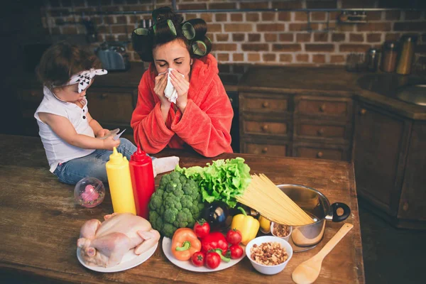 Mama stresată acasă. Mamă tânără cu un copil mic în bucătăria casei. Femeia face multe sarcini în timp ce are grijă de copilul ei. Femeia e bolnavă şi are un nas curbat. . — Fotografie, imagine de stoc