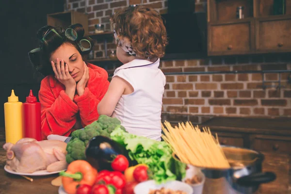 Stressed mum at home. Young mother with little child in the home kitchen. Woman doing many tasks while looks after her baby — Stock Photo, Image