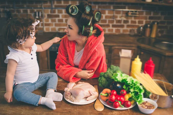 Mama acasă. Mamă tânără cu un copil mic în bucătăria casei. Femeia face multe sarcini în timp ce are grijă de copilul ei — Fotografie, imagine de stoc