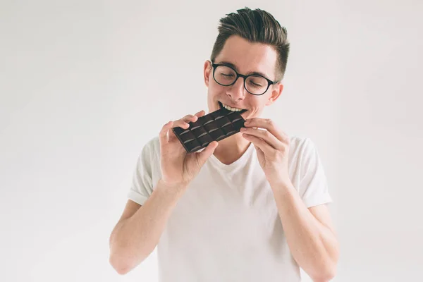 Junger Mann beim Essen einer Schokoriegel. Nerd trägt Brille. — Stockfoto