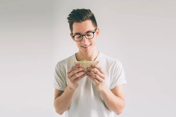 Muž, který držel kus hamburgeru. studentka jí rychlého občerstvení. není užitečné potravin. velmi hladový muž. Nerd má na sobě brýle. — Stock fotografie