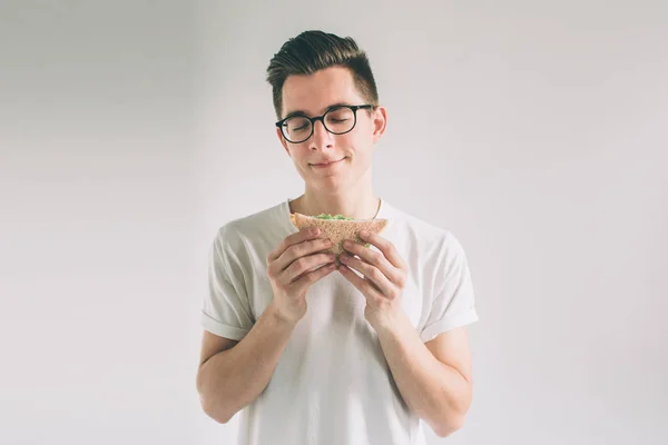 햄버거 한 조각을 들고 남자입니다. 학생은 패스트 푸드를 먹는다. 도움이 안 음식. 매우 배고픈 사람입니다. 괴상 한 안경을 쓰고는. — 스톡 사진