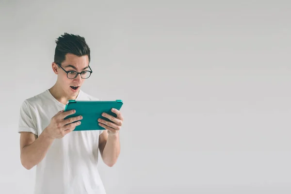 Nerd is wearing glasses holds the white empty screen tablet device. A man in a white T-shirt is standing on a white background — Stock Photo, Image