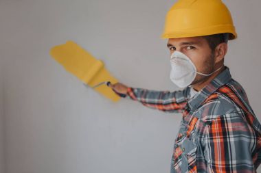 Builder inşaat alanında çalışır ve tavan ölçer. Bir işçi turuncu bir kask ve bir rulo duvar boyaları.