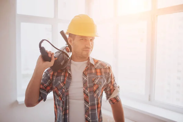 Hält der Arbeiter oder Bauarbeiter eine Tasse Kaffee in der Hand und blickt auf das Tablet. vor dem Hintergrund von Bau und Reparatur. — Stockfoto