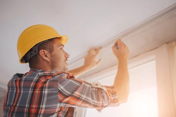 Строитель работает на строительной площадке и измеряет потолок. Рабочий в оранжевом строительном шлеме делает ремонт в доме . — стоковое фото