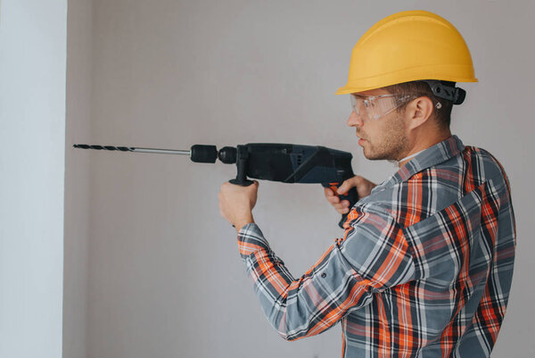 Builder worker with equipment making hole in wall at construction site