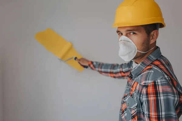 Строитель работает на строительной площадке и измеряет потолок. Работник в оранжевом шлеме и в краске на стене. . — стоковое фото