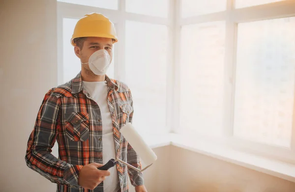 Der Bauarbeiter arbeitet auf der Baustelle und misst die Decke. Ein Arbeiter mit orangefarbenem Helm und Farbrolle bemalt die Wand. — Stockfoto