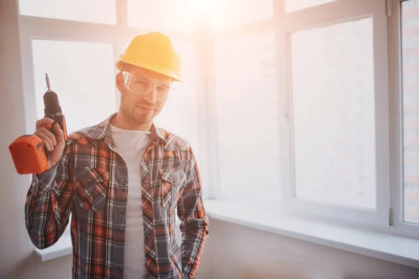 Der Arbeiter oder Bauarbeiter hält eine elektrische Bohrmaschine in der Hand. Bau- oder Reparaturkonzept. vor dem Hintergrund der Bautätigkeit — Stockfoto