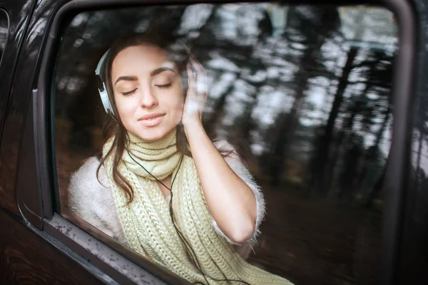 Femme dans la voiture, concept d'automne. Jolie fille souriante écoutant de la musique sur votre smartphone avec des écouteurs se déplaçant en voiture . — Photo