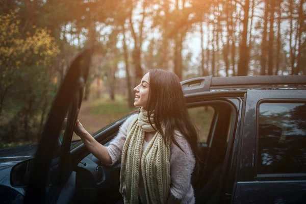 Long-haired brunette on the auto background. A female model is wearing a sweater and a scarf. Autumn concept. Autumn forest journey by car — Stock Photo, Image