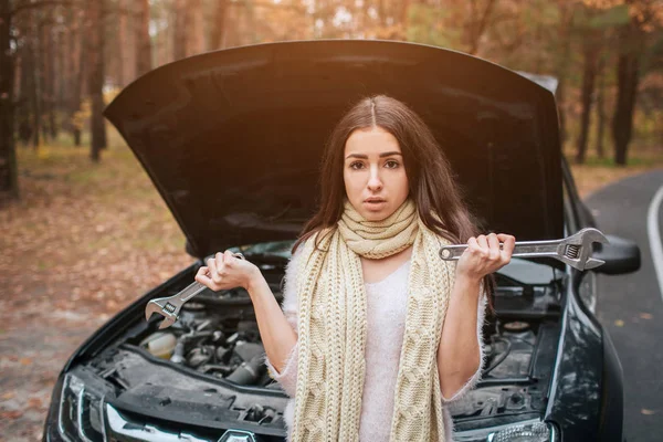 Mylić, młoda kobieta, patrząc na podziale samochód silnik naprawy samochodu na ulicy posiada klucz — Zdjęcie stockowe