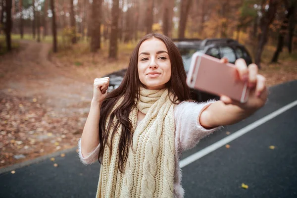 Piękna kobieta sprawia, że selfie. Dziewczyna jest za pomocą smartfona. Zbliżenie dłoni. Koncepcja jesień. Jesień las podróż samochodem. — Zdjęcie stockowe