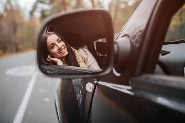 Langhaarige Brünette auf dem Auto-Hintergrund. Ein weibliches Model trägt einen Pullover und einen Schal. Herbstkonzept. Herbstliche Waldfahrt mit dem Auto — Stockfoto