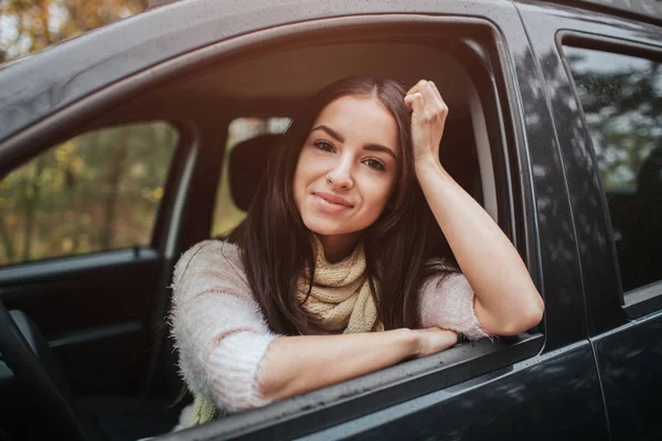 Długowłosy Brunetki na tle auto. Modelki ma na sobie sweter i szalik. Koncepcja jesień. Jesień las podróż samochodem — Zdjęcie stockowe