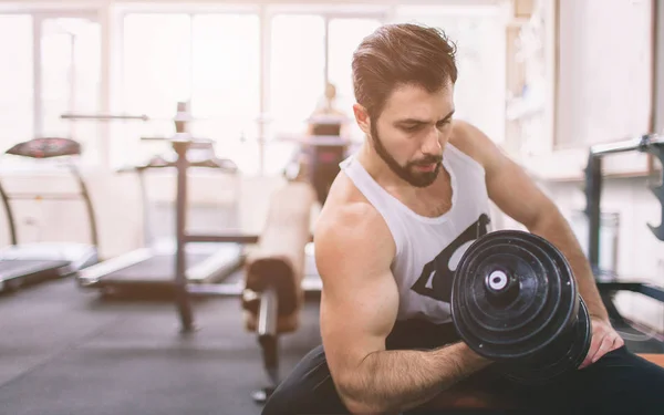 Uomo barbuto muscolare durante l'allenamento in palestra. Atleta bodybuilder muscolare in palestra allenamento bicipiti con manubrio. Fitness indoor — Foto Stock