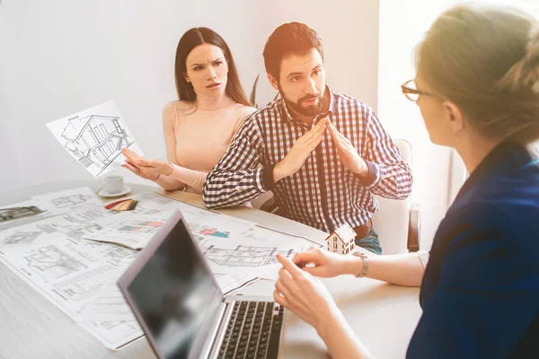 Familia joven pareja compra propiedades de alquiler de bienes raíces. Agente dando consulta a hombres y mujeres. Firma del contrato para la compra de casa o piso o apartamentos. El dilema de la elección. Gesticulación con — Foto de Stock