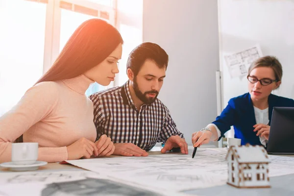 Familia joven pareja compra propiedades de alquiler de bienes raíces. Agente dando consulta a hombres y mujeres. Firma del contrato para la compra de casa o piso o apartamentos. Debate sobre el tamaño . — Foto de Stock