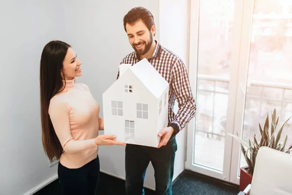 Familia joven pareja compra propiedades de alquiler de bienes raíces. Agente dando consulta a hombres y mujeres. Firma del contrato para la compra de casa o piso o apartamentos. Él tiene un modelo de la casa en las manos —  Fotos de Stock